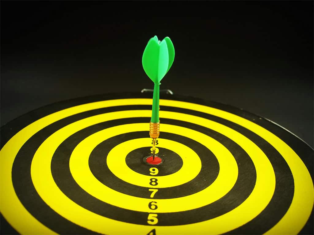 A yellow dart board with green dart in the bullseye